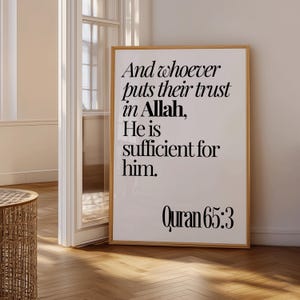 May include: A framed print with a light wood frame. The print has black text on a white background. The text reads "And whoever puts their trust in Allah, He is sufficient for him. Quran 65:3". The print is displayed in a room with a wooden floor.