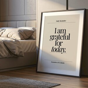 May include: A framed print with the text "I am grateful for today" in a bedroom setting. The print has a black frame and a neutral background. The words "Daily Reminder" and "Reminders of Gratitude" are also printed on the artwork.