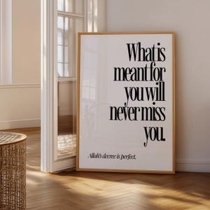 May include: A framed print with the text "What is meant for you will never miss you." The print is in a wooden frame and features a minimalist design with black text on a white background. The phrase "Allah's decree is perfect" is at the bottom.
