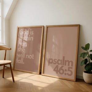 Puede incluir: Dos impresiones artísticas enmarcadas con marcos de madera. Una impresión tiene el texto "God is within her, she will not fall." La otra impresión tiene el texto "psalm 46:5." Las impresiones tienen un fondo rosa apagado.