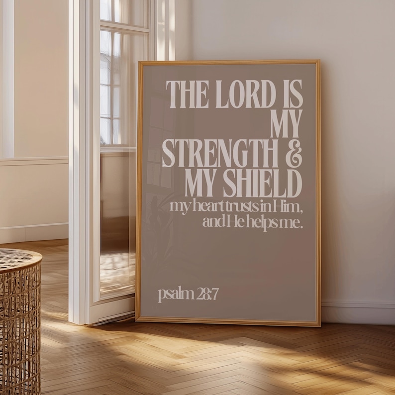Może przedstawiać: Oprawiony wydruk z białym tekstem "THE LORD IS MY STRENGTH & MY SHIELD" na szarobrązowym tle. Tekst zawiera r&oacute;wnież "my heart trusts in Him, and He helps me." i "psalm 28:7". Rama jest złota.