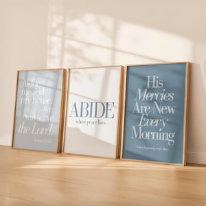 Op de afbeelding: Drie ingelijste kunstdrukken met inspirerende citaten. De prints tonen tekst in wit en lichtblauw op een witte en blauwe achtergrond. De frames hebben een licht houten kleur. De citaten zijn onder meer "ABIDE where peace lives."