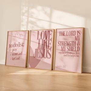 Könnte beinhalten: Drei gerahmte Kunstdrucke mit goldenen Rahmen. Die Drucke zeigen inspirierenden Text in Mauve auf hellrosa Hintergrund. Der Text enthält Sätze wie "Love Like Jesus" und "The Lord is My Strength & My Shield."