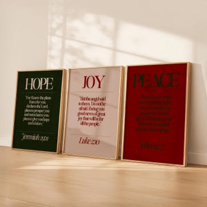 May include: Three framed art prints with the words "HOPE", "JOY", and "PEACE". Each print has a gold frame. The "HOPE" print is dark green with white text, "JOY" is light pink with red text, and "PEACE" is red with white text. Inspirational wall art.