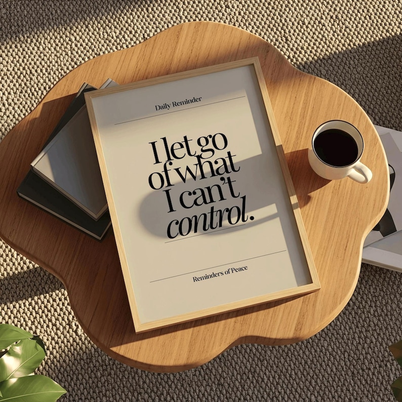 May include: A framed print with the text "I let go of what I can't control" in a minimalist design. The print is on a wooden table with a coffee cup and books.
