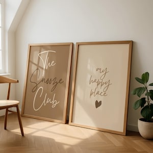 Pode incluir: Duas impress&otilde;es art&iacute;sticas emolduradas com molduras de madeira. Uma impress&atilde;o tem o texto "The Snooze Club" em estilo manuscrito sobre um fundo castanho. A outra impress&atilde;o tem o texto "my happy place" com um cora&ccedil;&atilde;o sobre um fundo creme.