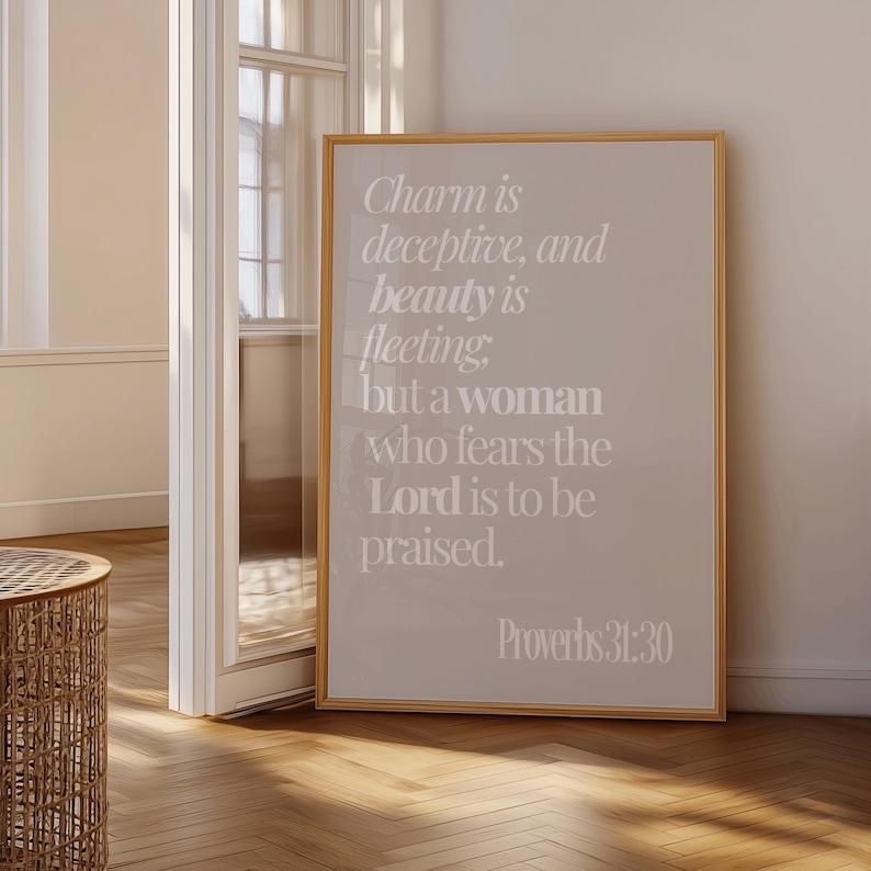 Może przedstawiać: Oprawiony wydruk z tekstem "Charm is deceptive, and beauty is fleeting; but a woman who fears the Lord is to be praised. Proverbs 31:30" w jasnobeżowym kolorze. Rama jest w kolorze jasnobrązowym.