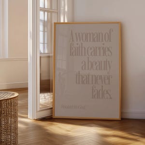 Może przedstawiać: Oprawiony wydruk z beżowym tłem i złotą ramą. Wydruk zawiera tekst "A woman of faith carries a beauty that never fades". Słowa "Rooted in God" znajdują się na dole. Wydruk jest eksponowany w pokoju z drewnianą podłogą.