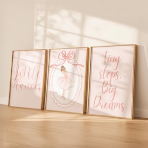 Könnte beinhalten: Drei gerahmte Kunstdrucke mit goldenen Rahmen. Die Drucke zeigen rosa Hintergründe mit Text und Illustrationen. Ein Druck sagt "Little dancer", ein anderer hat eine Ballerina-Illustration, und der dritte sagt "Tiny steps. Big Dreams."