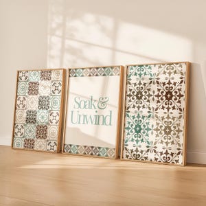 Puede incluir: Tres impresiones artísticas enmarcadas con marcos de madera. Las impresiones presentan patrones de baldosas decorativas en tonos marrón, verde azulado y blanco. La impresión central tiene el texto "Soak & Unwind" en verde azulado suave.