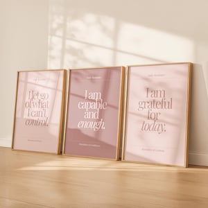 Puede incluir: Tres impresiones artísticas enmarcadas con citas inspiradoras en un estilo minimalista. Las impresiones presentan frases como "Soy capaz y suficiente" y "Estoy agradecido por hoy" en una paleta de colores suaves y apagados con marcos dorados.