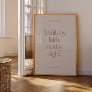 Może przedstawiać: Oprawiony wydruk z tekstem "Walk by faith, not by sight." w miękkim, neutralnym kolorze. Wydruk zawiera r&oacute;wnież tekst "Daily Reminder" i "2 Corinthians 5:7". Rama jest w jasnym kolorze drewna.