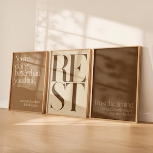 May include: Three framed art prints with inspirational quotes. The frames are a light brown color. The first print says "You're doing better than you think" in a light brown color. The second print says "REST" in a dark brown color. The third print says "Trust the timing."