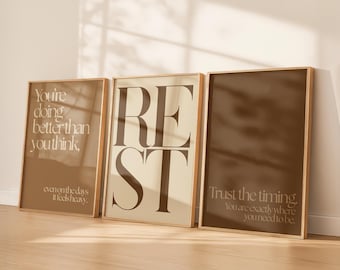 May include: Three framed art prints with inspirational quotes. The frames are a light brown color. The first print says "You're doing better than you think" in a light brown color. The second print says "REST" in a dark brown color. The third print says "Trust the timing."
