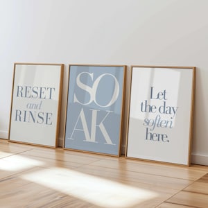 May include: Three framed art prints with inspirational text. The prints have a light blue and white color scheme. The first print says "RESET and RINSE", the second says "SOAK", and the third says "Let the day soften here."