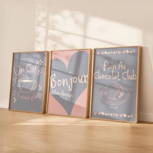 May include: Three framed prints with gold trim. The prints feature French phrases and illustrations: "Un Café, S'il vous plaît!" with a coffee cup, "Bonjour Mon Amour!" with a heart, and "Pain Au Chocolat Club" with a croissant.