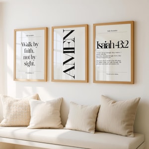 K&ouml;nnte beinhalten: Drei gerahmte Kunstdrucke mit inspirierenden Zitaten. Die Drucke haben einen hellen Holzrahmen und einen wei&szlig;en Hintergrund mit schwarzem Text. Der erste Druck lautet "Walk by faith, not by sight". Der zweite Druck lautet "AMEN". Der dritte Druck lautet "Jesaja 43:2".