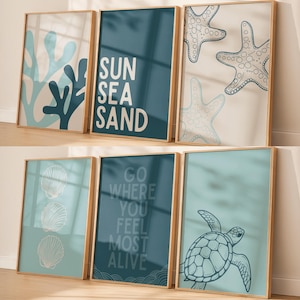Könnte beinhalten: Sechs gerahmte Kunstdrucke mit Strandmotiv. Die Drucke zeigen Bilder von Korallen, Seesternen, Muscheln und einer Meeresschildkröte. Ein Druck trägt die Worte "SUN SEA SAND", ein anderer "GO WHERE YOU FEEL MOST ALIVE". Die Rahmen sind hellbraun.