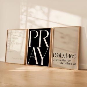 May include: Three framed art prints with inspirational quotes. One print features the word "PRAY" in large white letters on a black background. The other two prints have text on a beige background, with gold frames.