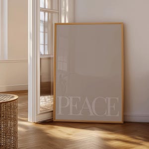 Może przedstawiać: Oprawiony wydruk ścienny z napisem "PEACE" dużymi, jasnymi literami. Grafika ma neutralną paletę kolor&oacute;w, z beżowym tłem i drewnianą ramą. Wydruk jest eksponowany w dobrze oświetlonym pomieszczeniu z drewnianą podłogą.