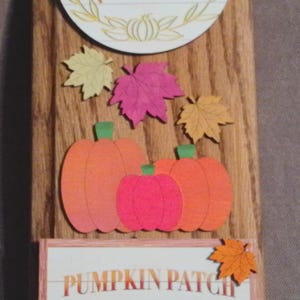 May include: Wooden sign with a fall theme. The sign features a round element with the text "Hey there Pumpkin", pumpkins, and a red truck with pumpkins in the back. Decorative maple leaves in orange, pink, and yellow are also included.