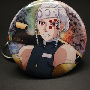 May include: Round button featuring a character from an anime series. The character has white hair, red eyes, and a distinctive facial marking. The button has a metallic silver ring and a colorful background. The character is wearing a dark blue uniform.