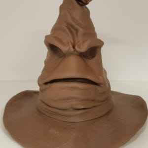 May include: A brown Sorting Hat, a character from the Harry Potter series, with a wide brim and a pointed top. The hat has a face with a mouth and eyes, and is made of a textured material.