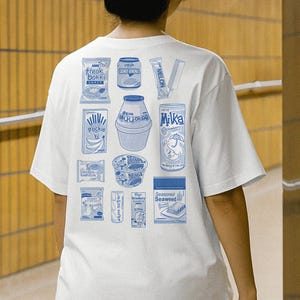 May include: White t-shirt with a blue graphic print of various snacks and drinks, including tteok bokki, rice soda, melon, Pockie, and Milka. The shirt features a crew neck and short sleeves.