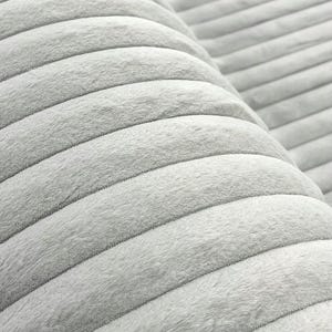 May include: Close-up of a soft, light gray corduroy fabric. The fabric has a ribbed texture with parallel, raised lines. The material appears plush and inviting, suggesting comfort and warmth. Ideal for upholstery, clothing, or home decor projects.