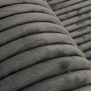 May include: Close-up of a gray, corduroy fabric with a ribbed texture. The fabric has a soft, plush appearance and is folded over, revealing the texture and depth of the material. The color is a muted, neutral gray.