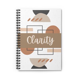 May include: Spiral-bound notebook with a white cover featuring a geometric design in shades of brown, beige, and black. The word "Clarity" is written across the center in a cursive font. The notebook is designed for writing and note-taking.