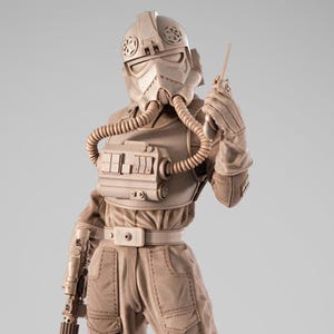 May include: A tan-colored 1/6 scale figurine of a character in a helmet and uniform, holding a blaster and a communication device. The figure stands on a detailed hexagonal platform with a circular emblem. The base has the text "SW3D PATREON".