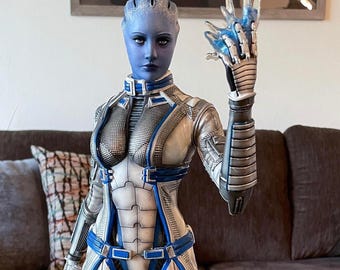 Op de afbeelding: Gedetailleerd beeldje van een blauwhuidig ​​mensachtig personage in een futuristisch outfit. Het beeldje is overwegend wit en zilver, geaccentueerd met blauwe lijnen en details. Het staat op een cirkelvormige basis met een gestileerd embleem, één hand omhoog.