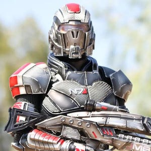 以下が含まれることがあります： 黒と銀のアーマーに赤いアクセントが施された、未来的な兵士の精巧なアクションフィギュア。フィギュアは赤いディテールが施された大きな銃を持っています。フィギュアは黒い台座の上に立っています。