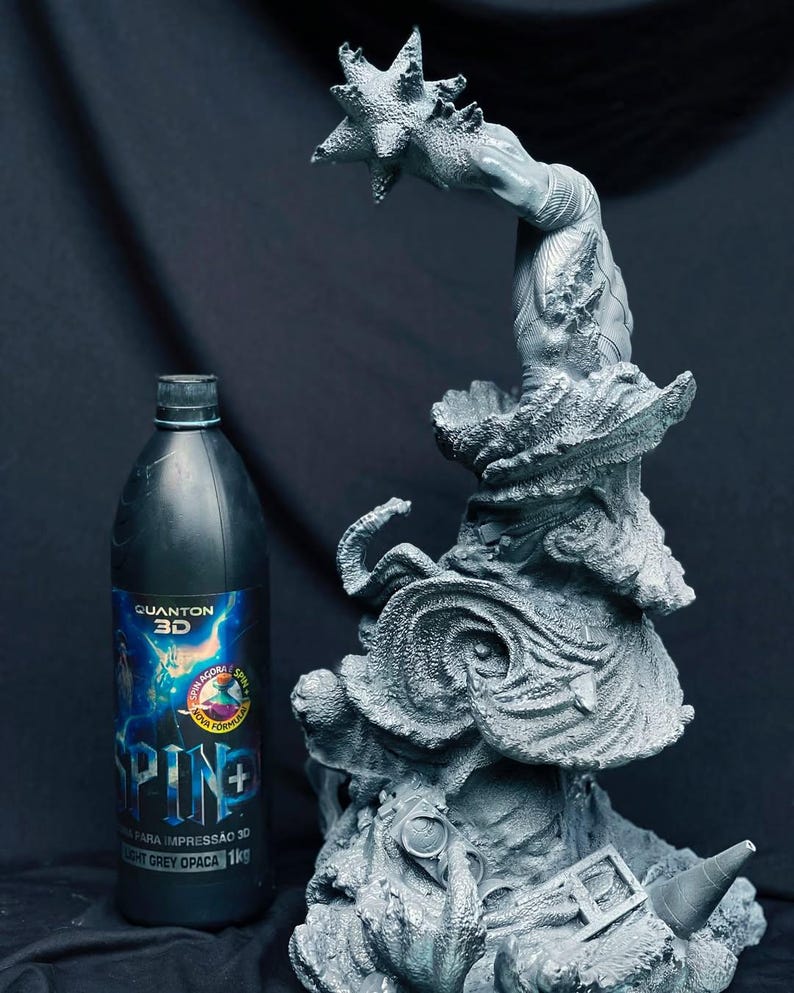 Pu&ograve; includere: Una scultura grigia stampata in 3D di una creatura fantastica con una mano a forma di stella, accanto a una bottiglia nera con un'etichetta blu e bianca. La bottiglia ha testo in portoghese. La scultura presenta dettagli e trame intricati.