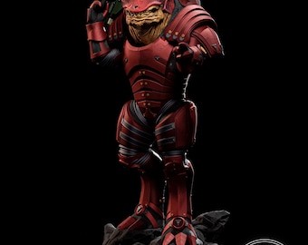 Op de afbeelding: Rood en zwart beeldje van een fictieve alien-krijger met een geweer. De figuur staat op een rotsachtige basis tegen een zwarte achtergrond. De alien heeft een getextureerd, geelbruin gezicht en draagt rode bepantsering.