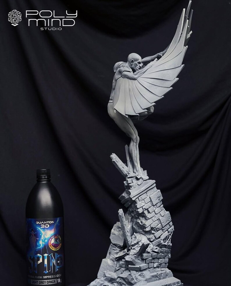 May include: A gray sculpture of a figure with large wings, perched atop a crumbling brick structure. The figure is holding the wings open. A black bottle with text is in the foreground. The sculpture is a detailed art piece.