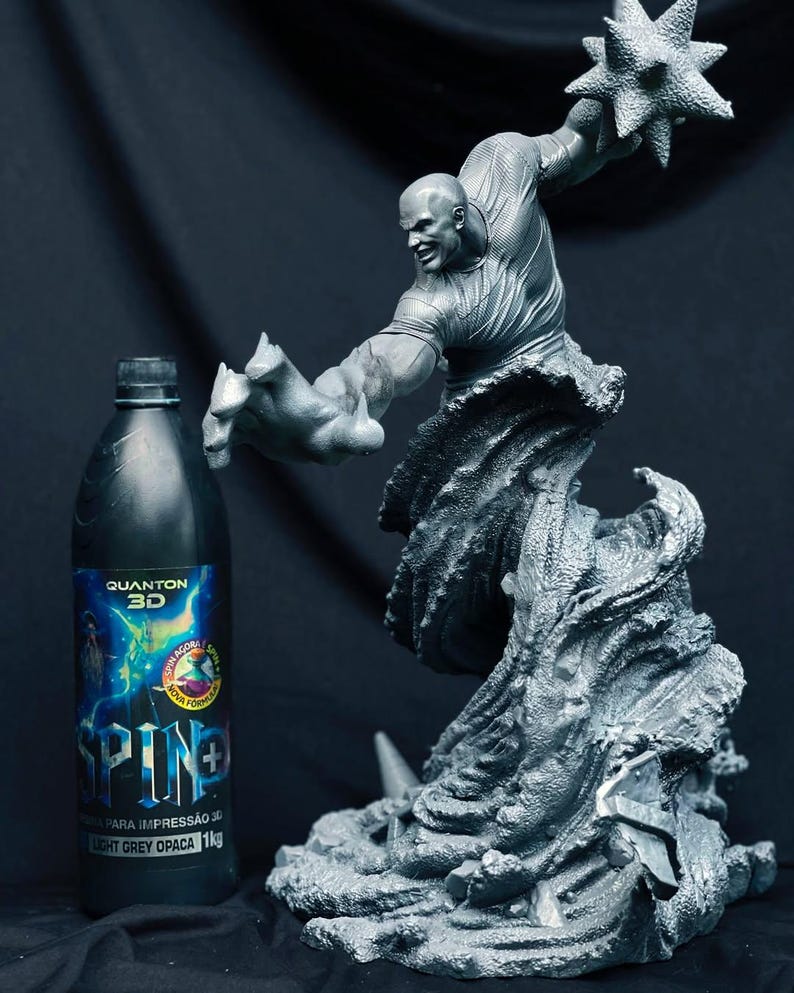 Pu&ograve; includere: Scultura grigia stampata in 3D di una figura muscolosa in posa dinamica, che tiene una palla spinosa. Accanto, una bottiglia nera con il testo "QUANTOM 3D" e "SPINE+". Sfondo scuro.