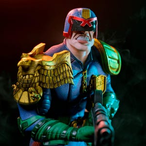 May include: A detailed figurine of Judge Dredd, a comic book character, in a blue uniform with green accents. The figure has a stern expression, a helmet with a red X, and gold shoulder armor. The figure is holding a black weapon.