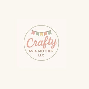 May include: A circular logo with the word "Crafty" in a soft pink script font, above "AS A MOTHER" and "LLC" in a smaller, gray font. A banner of pastel-colored flags sits above the word "Crafty". The logo is set against a cream-colored background.