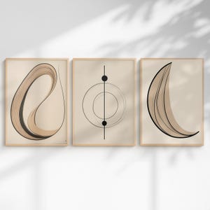 以下が含まれることがあります： 3つの額入り抽象芸術プリントのセット。各プリントは、ミニマリストの黒とタンのラインアートデザインを備えたベージュの背景が特徴です。フレームは明るい木の色で、全体的な美学はモダンでニュートラルです。