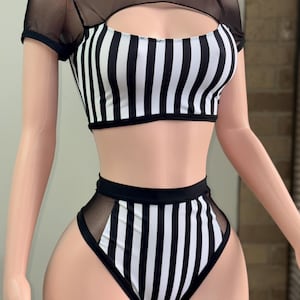 May include: A two-piece swimsuit featuring a black and white vertical striped pattern. The top has short sheer black mesh sleeves and a cutout neckline. The high-waisted bottom includes black mesh side panels that match the top's design elements.