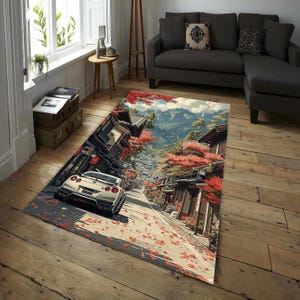May include: Rectangular area rug featuring a Japanese street scene with a white sports car. The rug depicts a road lined with traditional buildings and vibrant red autumn foliage. The background shows mountains and a blue sky.