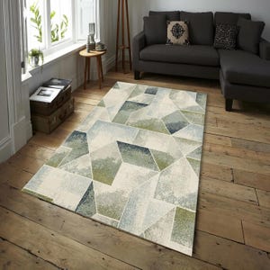 Könnte beinhalten: Ein rechteckiger Teppich mit geometrischem Design. Der Teppich zeigt ein Muster aus sich überlappenden Formen in Grün-, Blau- und Grautönen auf cremefarbenem Hintergrund. Der Teppich liegt auf einem Holzboden in einem Wohnzimmer.