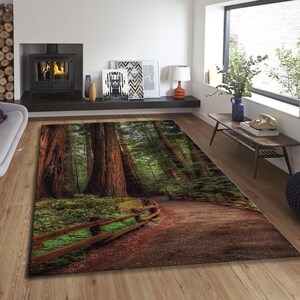 May include: A rectangular area rug featuring a forest scene with tall redwood trees, a wooden fence, and a path. The rug has a brown and green color palette, creating a natural and inviting aesthetic. The rug is placed on a wooden floor.