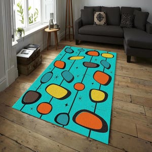 Puede incluir: Una alfombra rectangular con un diseño moderno de mediados de siglo. La alfombra presenta un fondo turquesa con líneas negras y formas abstractas coloridas en naranja, amarillo, marrón y verde azulado. La alfombra está colocada sobre un suelo de madera.