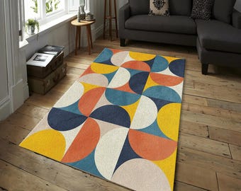 Pode incluir: Um tapete geométrico colorido com um design retro. O tapete apresenta um padrão de semicírculos sobrepostos em tons de amarelo, laranja, azul e creme. O tapete está colocado sobre um chão de madeira numa sala de estar, adicionando cor.