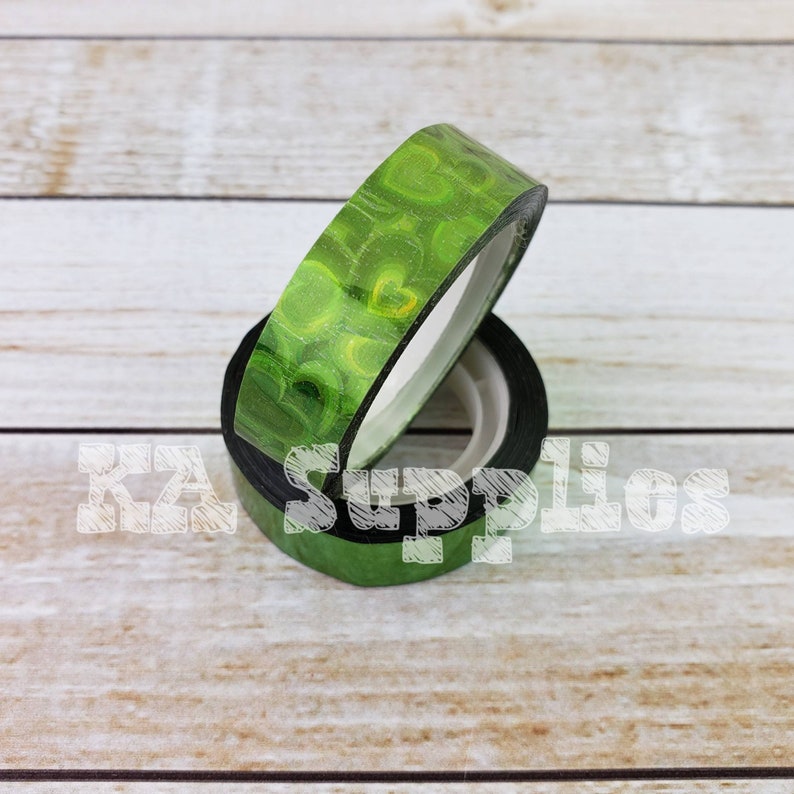May include: Two rolls of green washi tape with a holographic heart pattern. The tape is rolled up and the ends are visible.