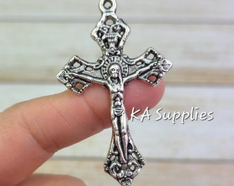 May include: Silver-toned crucifix pendant with intricate detailing. The cross features a figure of Jesus and ornate embellishments. The text "KA Supplies" is visible on the right side of the cross.