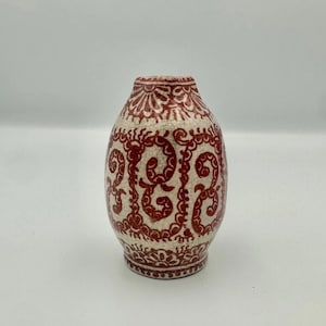 May include: A decorative ceramic vase with a cream-colored base and intricate red patterns. The vase has an oval shape and a detailed design that covers the entire surface, showcasing a blend of artistry and craftsmanship.